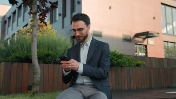 Hombre de negocios caucásico líder masculino empleador escribiendo mensaje en el teléfono móvil en la ciudad navegando por la red social uso de la aplicación de teléfono inteligente sonriente empresario de negocios fuera de la oficina mirando la sonrisa de la cámara - Metraje, vídeo