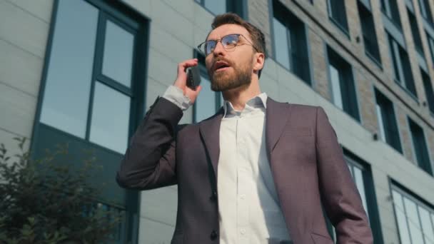 Kaukázusi dühös férfi vállalkozó férfi válasz hívás beszélgetés telefon vitatkozás a városban közelében iroda stresszes fickó irritált beszél frusztrált üzletember befejezni mobil beszélgetés vége üzleti konfliktus szabadban - Felvétel, videó