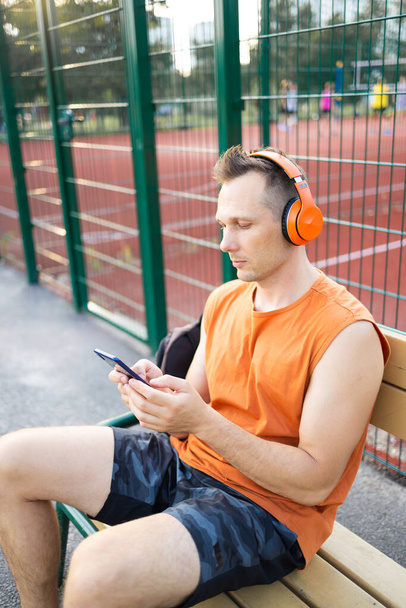 фітнес, спорт і концепція технології - молодий спортсмен з навушниками та смартфонами, що слухають музику на відкритому повітрі
 - Фото, зображення