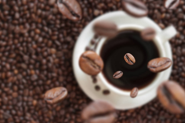 A kávébab beleesik egy csésze kávéba. Fehér csésze kávé a háttérben a kávébab. Energiaital, koffein. Szelektív fókusz - Fotó, kép