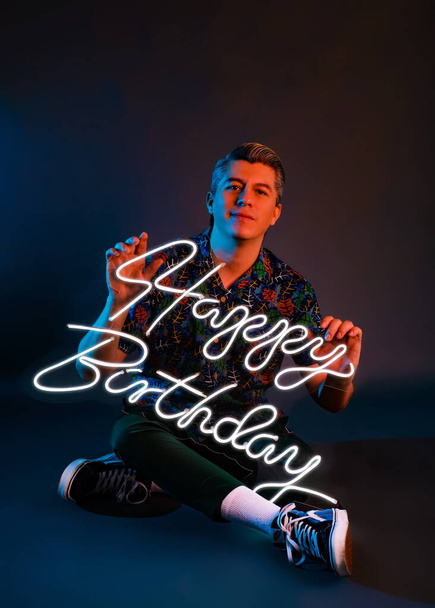Studio portrét s neonovými světly muže se zářivým nápisem Happy birthday. Muž slaví své narozeniny ve focení. - Fotografie, Obrázek