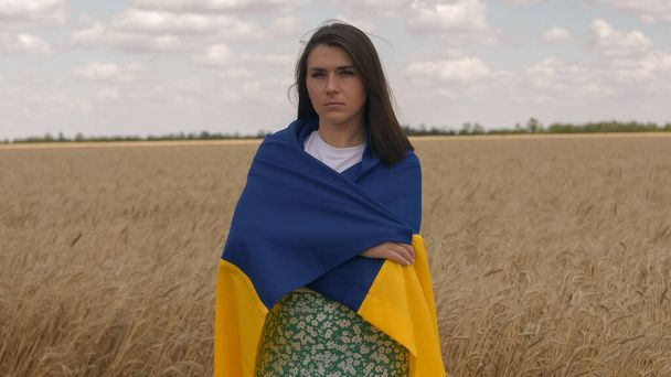 Portrét ukrajinské vlastenecké ženy stojí na pšeničném poli s modrožlutou vlajkou Ukrajiny - Fotografie, Obrázek