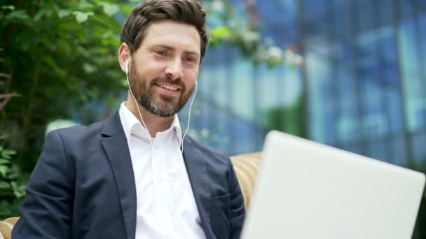 Handsome bearded businessman in suit working with laptop sitting on bench near modern office business center Happy Employee Executive typing browse laptop outside outdoors in city street Closeup smile - Footage, Video