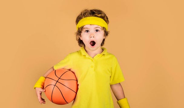 Aktív sport életmód, gyermekkor. Kosárlabda tréning gyerekeknek. Meglepett fiú kosárlabdával. Kis kosárlabdázó sportruházatban. Sportfelszerelés. Profi sport. Sport gyermekeknek - Fotó, kép