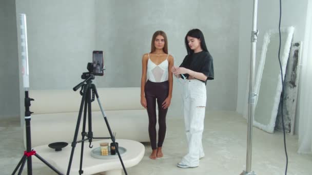Egy fiatal nő videót készít egy videó bloghoz az egészségről és a fogyásról, ami a karcsú modell mellett áll és méréseket végez a testén. Középső felvétel - Felvétel, videó