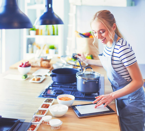 Young woman using a tablet computer to cook in her kitchen. - Foto, afbeelding