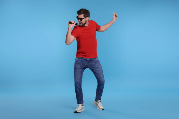 Handsome man with sunglasses and microphone singing on light blue background - Fotoğraf, Görsel