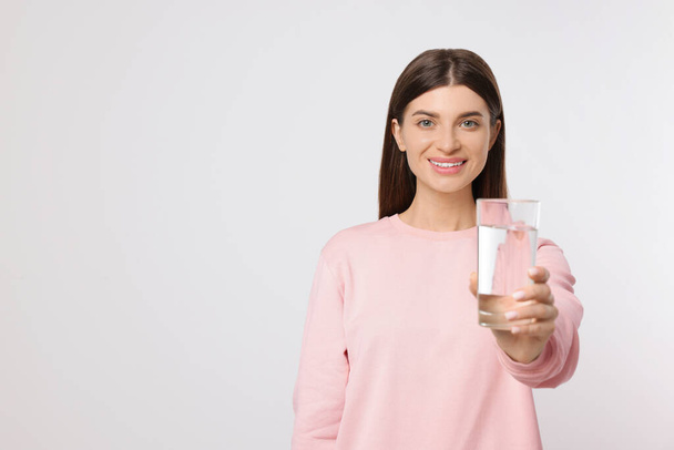 Healthy habit. Happy woman holding glass with fresh water on light grey background. Space for text - Valokuva, kuva