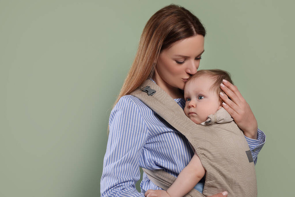 Mother holding her child in sling (baby carrier) on olive background. Space for text - Фото, зображення