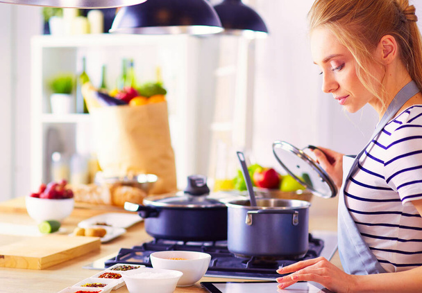 Young woman using a tablet computer to cook in her kitchen. - Foto, imagen