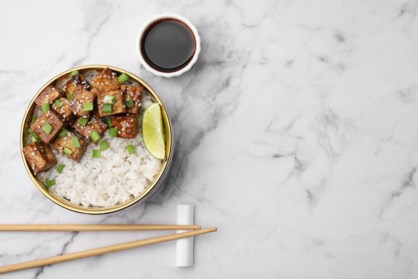 Delicious rice with fried tofu and green onions served on white marble table, flat lay. Space for text - Fotó, kép