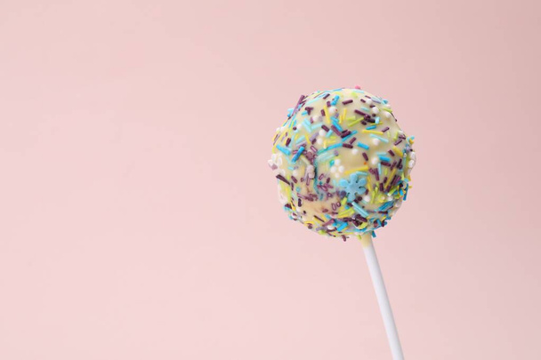 Delicious confectionery. Sweet cake pop decorated with sprinkles on pale pink background, closeup. Space for text - Фото, зображення