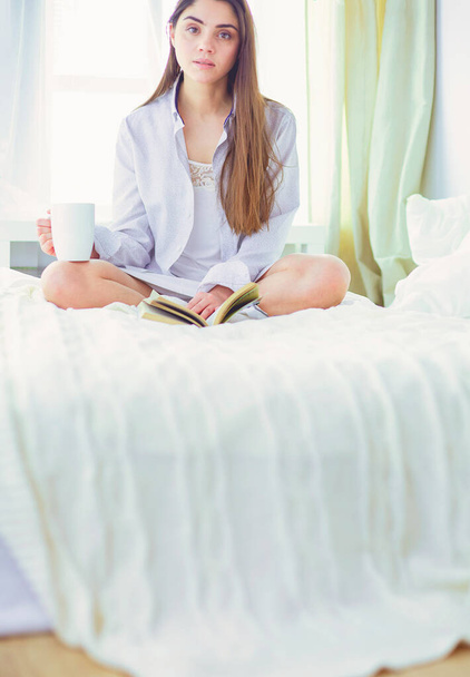 Woman sitting in bed reading a book and having breakfast. - Foto, afbeelding