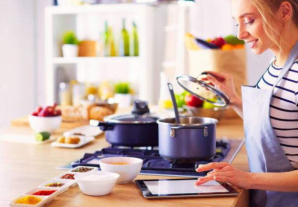 Young woman using a tablet computer to cook in her kitchen. - Photo, Image
