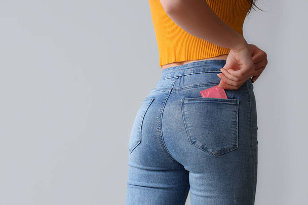 Young woman with condom in pocket on light background, back view - Photo, Image