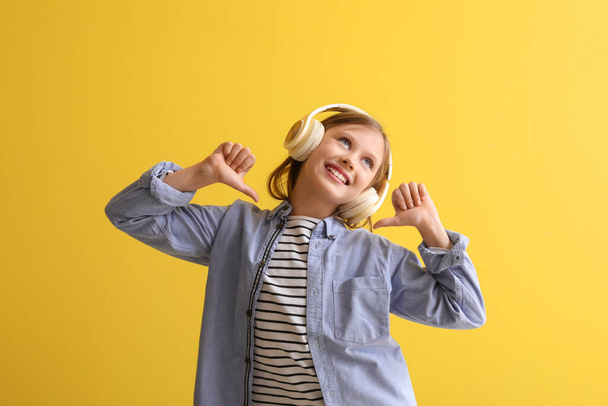 Little girl in headphones pointing at herself on yellow background - Foto, afbeelding
