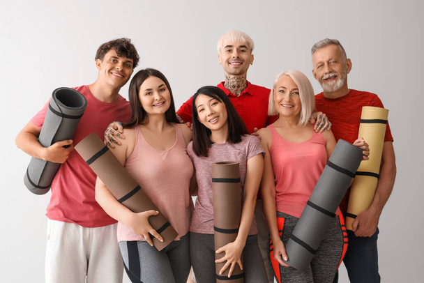Group of sporty people with fitness mats on light background - Fotó, kép