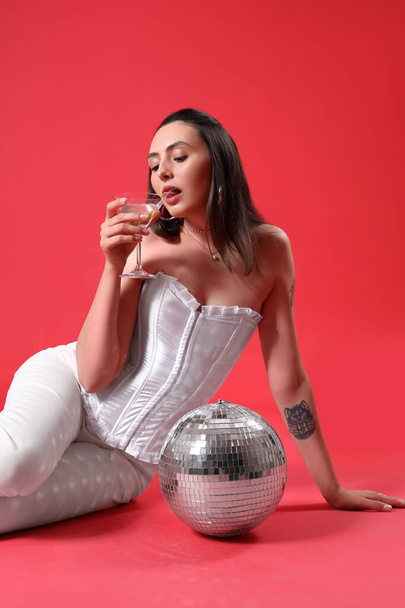 Beautiful woman with martini and disco ball on red background - Photo, Image
