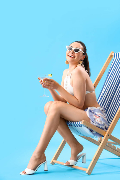 Beautiful woman in swimsuit with martini in deck chair on blue background - Φωτογραφία, εικόνα