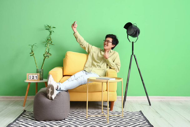 Jonge Aziatische man met mobiele telefoon het nemen van selfie op zijn vrije dag thuis - Foto, afbeelding