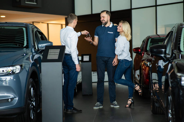 The seller hands over the car keys to the buyers. The couple bought a new car - Фото, зображення