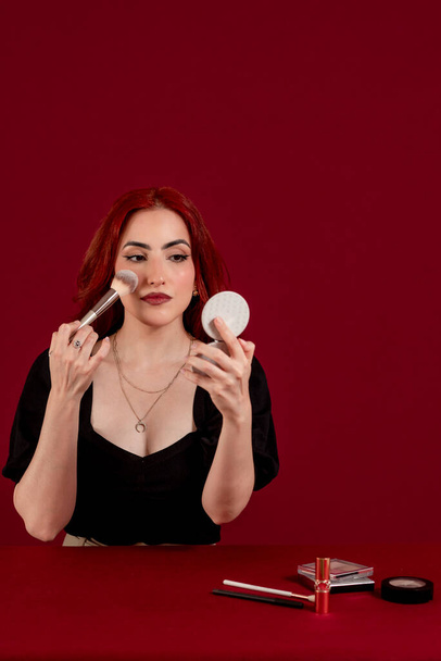 Stylish woman applying makeup on her face with a makeup brush against a colored isolated background. Beauty and cosmetic concept. - Φωτογραφία, εικόνα