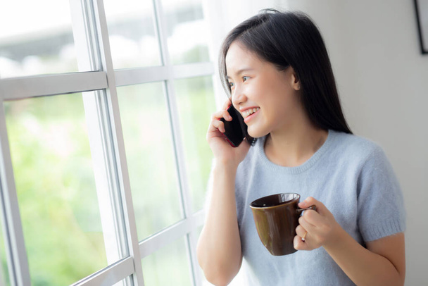 Happiness young asian woman talking with smartphone in the living room at home, female speaking with smart phone and hold coffee cup while relax and cozy at home, lifestyles and communication concept. - Foto, immagini