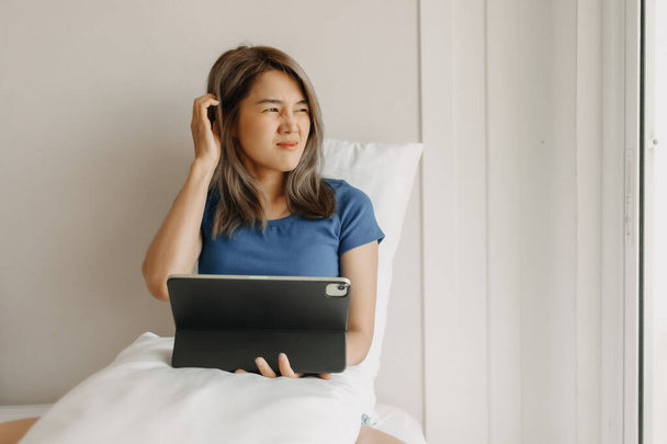 Asian woman works digital online on her bed feeling tired on vacation. - Φωτογραφία, εικόνα