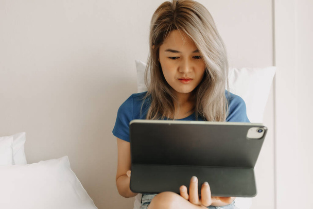 Serious asian woman working online with tablet on hotel bed in travel trip - Valokuva, kuva