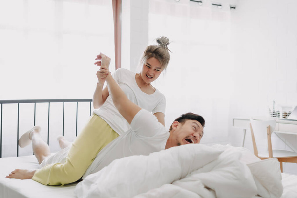 Funny asian couple wife giving husband hurt massage in white bedroom. - Photo, image