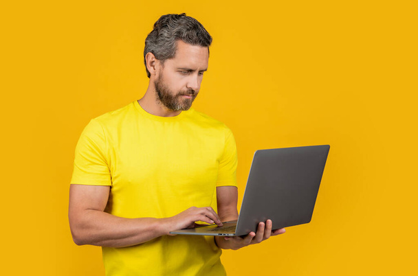 man blogger on background. man blogger in studio. photo of man blogger typing on laptop. man blogger isolated on yellow. - Foto, afbeelding