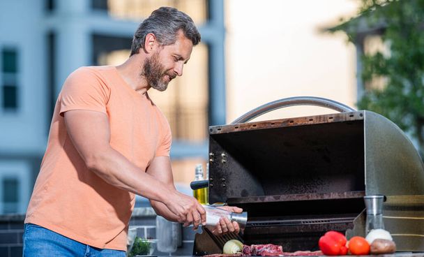 Man grilling steaks to perfection on smoky barbecue. Grilling man cook meat at barbecue. Grill sizzles with flavor. Outdoor man cooking grill and barbecue dishes. pork steak. - Фото, зображення