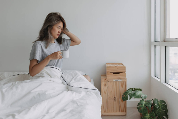 Asian woman hold a cup of coffee in white bedroom morning with empty space. - Foto, Imagen