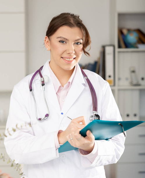Positive woman doctor is standing with documents in clinic - Foto, Imagem