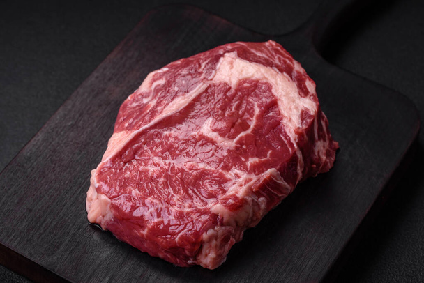 Fresh, raw beef steak with salt, spices and herbs on a dark textured background - Foto, imagen