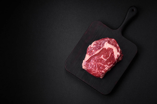 Fresh, raw beef steak with salt, spices and herbs on a dark textured background - Foto, Bild