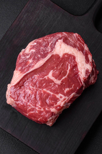 Fresh, raw beef steak with salt, spices and herbs on a dark textured background - Fotó, kép