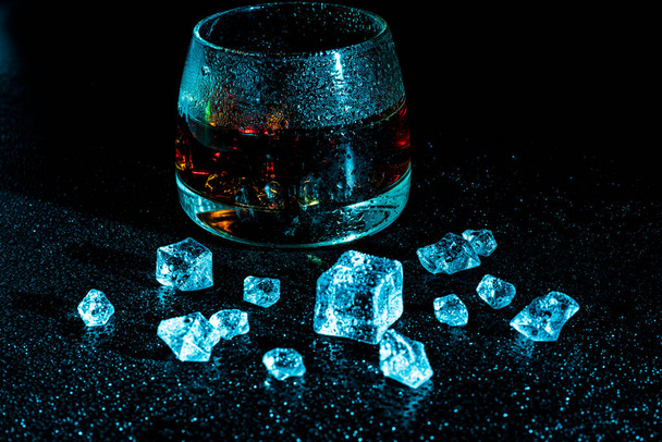 Glass with cognac and ice on a dark background. the concept of alcoholism and drinking - Photo, Image