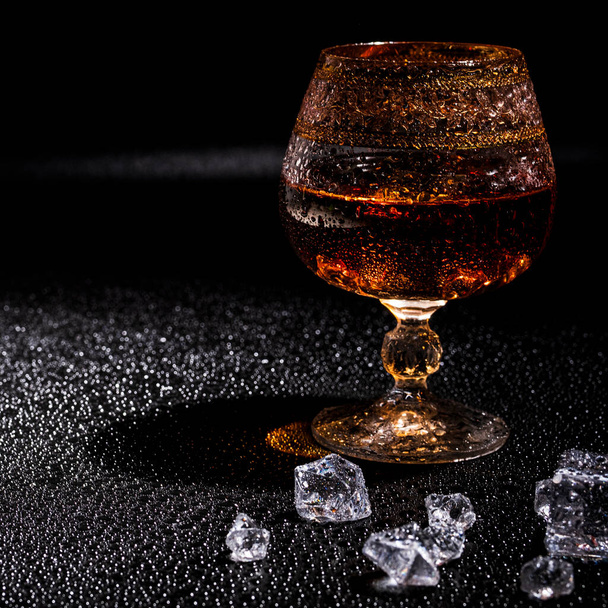Glas met cognac en ijs op een donkere achtergrond. het begrip alcoholisme en alcoholgebruik; - Foto, afbeelding