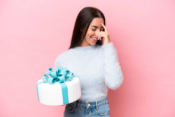 Young caucasian woman holding birthday cake isolated on pink background laughing - Photo, image