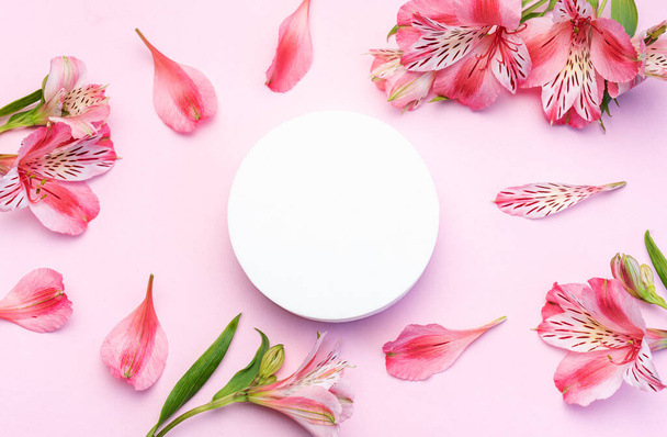 Leeg wit podium voor uw productpresentatie met alstroemeria bloemen op de roze achtergrond in een voorjaarsstemming. Vlakke lay, bovenaanzicht.  - Foto, afbeelding