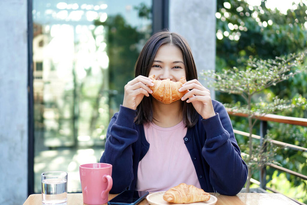 Mujer asiática sosteniendo un croissant en un café. - Foto, Imagen