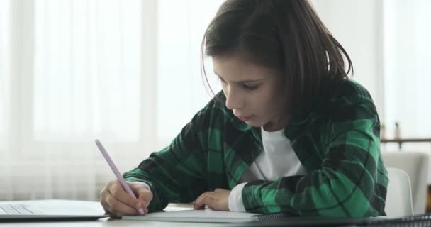 mladý kavkazský školák sedící za stolem v obývacím pokoji, plně zabraný do online lekce. S notebookem před sebou, se aktivně účastní, absorbuje znalosti. - Záběry, video