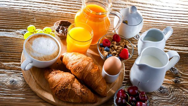 Ontbijt geserveerd met koffie, sinaasappelsap, croissants en ei. - Foto, afbeelding