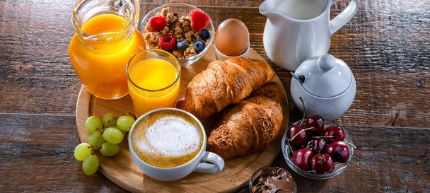 Ontbijt geserveerd met koffie, sinaasappelsap, croissants en ei. - Foto, afbeelding