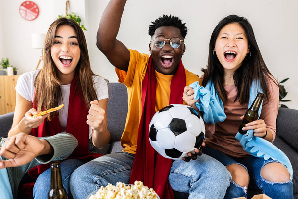 Diverse young friends watching a football match on TV at home. Sports entertainment concept. - Foto, Imagen