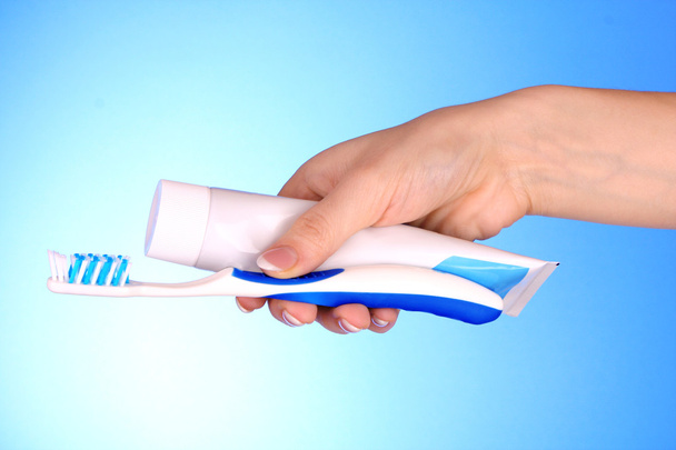 Tooth-paste and brush in the hand on blue background - 写真・画像