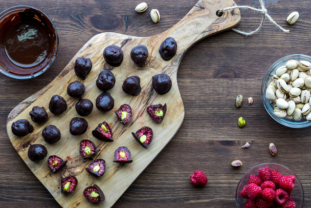 Prepared chocolate covered pistachio filled raspberries on a wooden board.  - Photo, Image