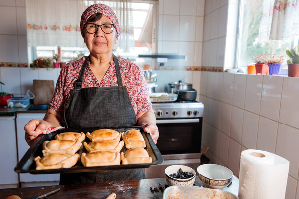Аромати спадщини: Латинська літня жінка готує чилійські запечені яловичі емпанади в теплі її домашньої кухні. Високоякісна фотографія - Фото, зображення