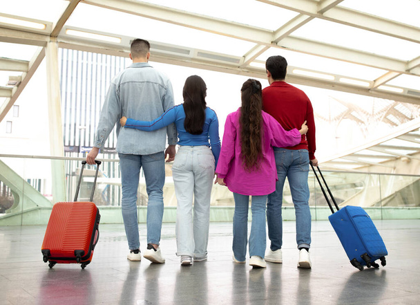 Arkadaşlarınla seyahat et. İki çiftin bavullarıyla durduğu, erkek arkadaşlarına sarılan, modern havaalanında tatilin ve seyahatin tadını çıkaran, birlikte uçmayı bekleyen genç kadınlar. - Fotoğraf, Görsel